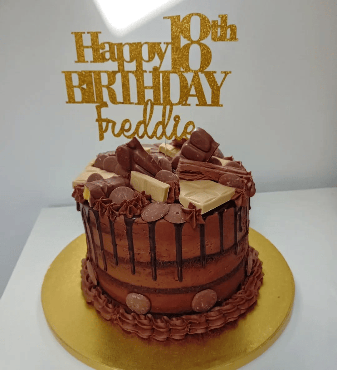 chocolate drip cake with custom text above and topped with chocolates
